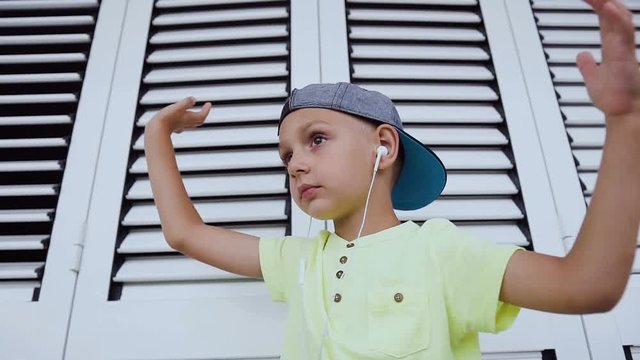 Caucasian little boy is listening to music and dancing gesturing with his hands. Portrait of a funny boy who dancing listen to good music in earphones from smartphone