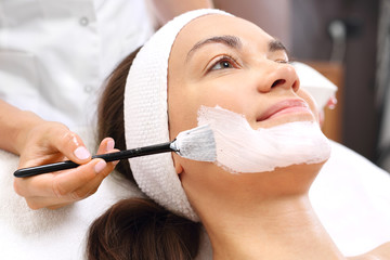 Pielęgnacja skóry, kosmetyczka nakłada maseczkę. Młoda kobieta w salonie kosmetycznym na zabiegu pielęgnacyjnym skóry twarzy.