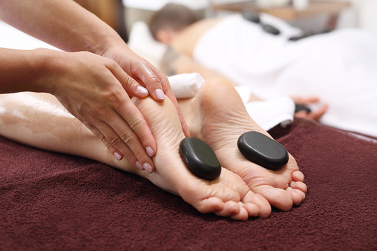 Masaż gorącymi kamieniami.  Kobiece stopy z kamieniami bazaltowymi, relaks w salonie spa.