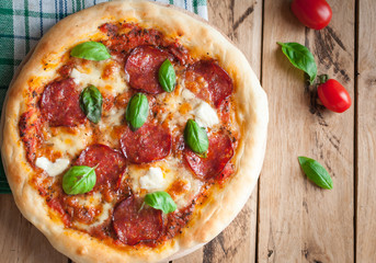 Close-up of homemade rustic pizza with salami, mozzarella and fresh basil, top view