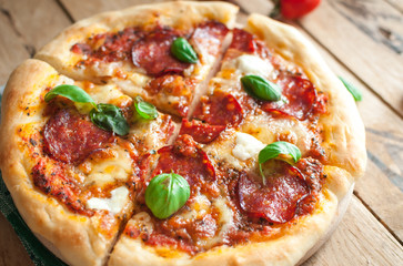 Close-up of homemade rustic pizza with salami, mozzarella and fresh basil on top