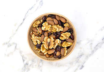 Delicious nuts arrangement in a wooden bowl. Close up shot of various nuts, healthy eating scene and marble background. Top view.