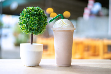 Chocolate frappe and whipping cream topping in plastic disposable glass on the wood table in cafe.