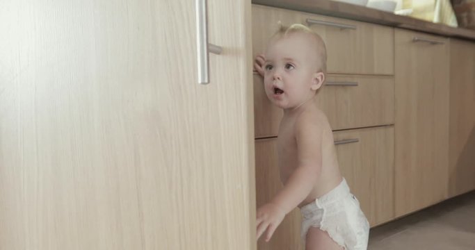 Toddler child in kitchen opens wood cabinet
