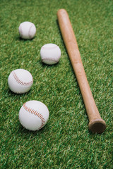 close up view of baseball bat and balls arranged on green lawn