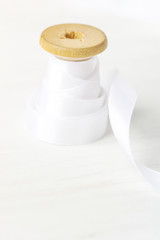Single Wooden Spool Roll with Curly Silk Ribbon on White Wood Background. Sewing Crafts Hobby Concept. Elegant Styled Stock Image for Social Media Blog Website Workshop Announcement. Copy Space