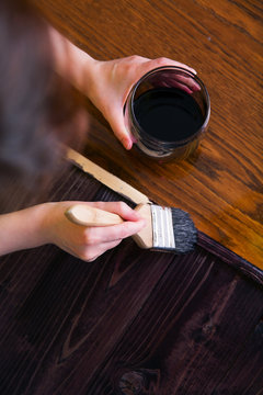 A woman paints by hand the planks of stained ebony wood.