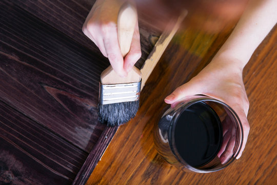 A woman paints by hand the planks of stained ebony wood. Top view