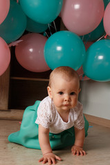 Fototapeta na wymiar A small, charming child, a girl, celebrates her first birthday, sitting next to her with balloons. Children's Party Organization.