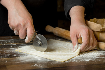 Chef cutting dough for pasta on wooden table with a rolling pin, flour in a paper bag and chopped pasta. Top view, concept of home cooking recipe book.