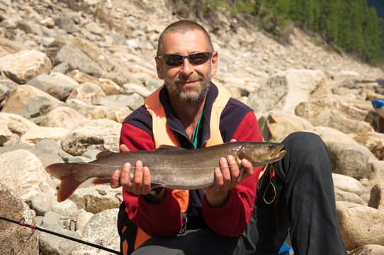 Fisherman caugth a small taimen in wild Siberian river.