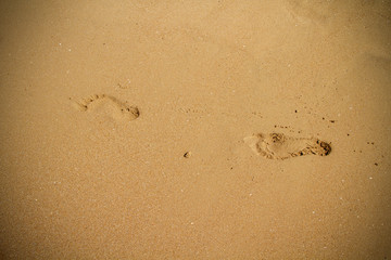 Fototapeta na wymiar Background with two Footprints of a man in the sand. Traces of an adult male on the sand. Footprints from the feet of a man. A footprint of a man on the beach near the surf.