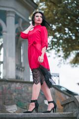 Attractive brunette woman in red dress walking in the town in cloudy day