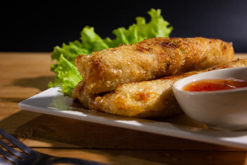 Fried spring rolls with chili sauce on wooden table.