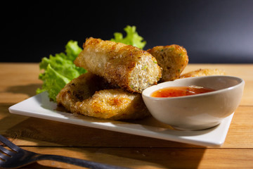 Fried spring rolls with chili sauce on wooden table closeup.