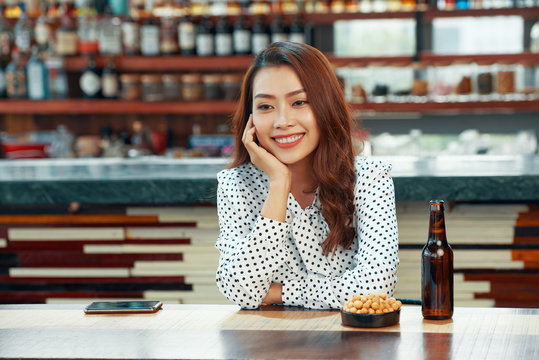 Pretty Vietnamese woman drinking beer and eating snacks in bar