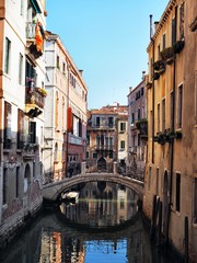 Fototapeta na wymiar The canal is surrounded with the bridge by ancient buildings, gondolas and boats in Venice