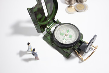 Miniature businessman with compass and coins closeup top view.