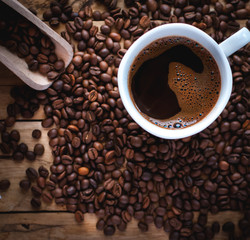 Close-up of black coffee in white cup, with coffee beans on wooden background, top view