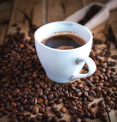 Close-up of black coffee in white cup, with coffee beans on wooden background