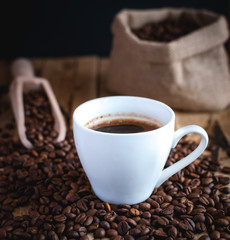 Close-up of black coffee in white cup, with coffee beans on wooden background