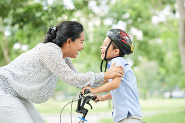 Happy mother congratulating her son with first bicycle ride