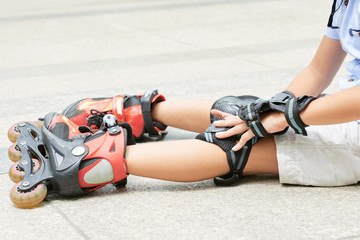 Fototapeta na wymiar Girl in roller skates sitting on ground with pain in her knee