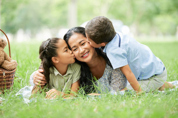 Boy and girl kissing their mother on both cheeks at picnic in park