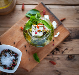 Close-up of marinated feta cheese in olive oil, herbs and red pepper flakes on wooden background, top view