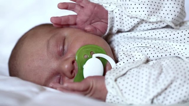 Newborn baby sleeps with pacifier in his mouth. Little 2 weeks old newborn boy lies on the bed. Asleep newborn baby boy