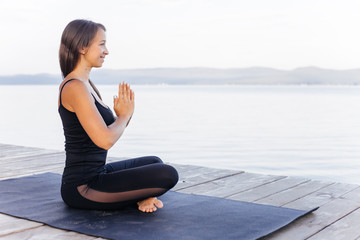 Fototapeta na wymiar Young attractive smiling woman practicing yoga on a lake