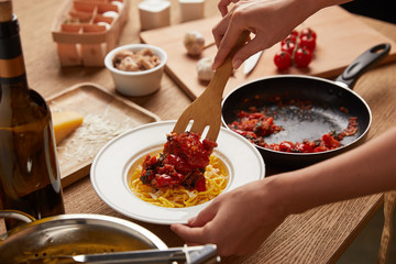 cropped shot of woman putting tomatoes from frying pan onto spaghetti in plate