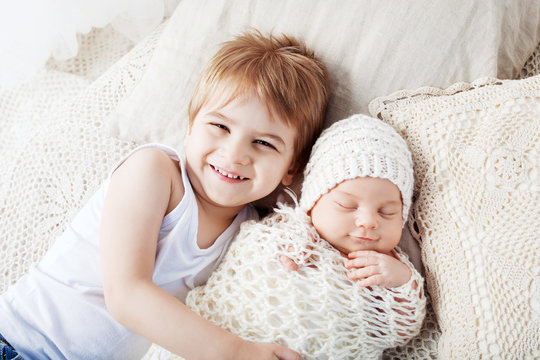 Portrait of newborn baby and elder brother. Smiling young boy lying with newborn brother.