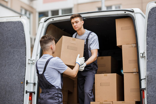 Two young handsome movers wearing uniforms are unloading the van