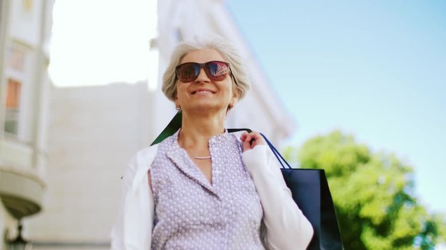 sale, consumerism and people concept - senior woman with shopping bags walking along city street