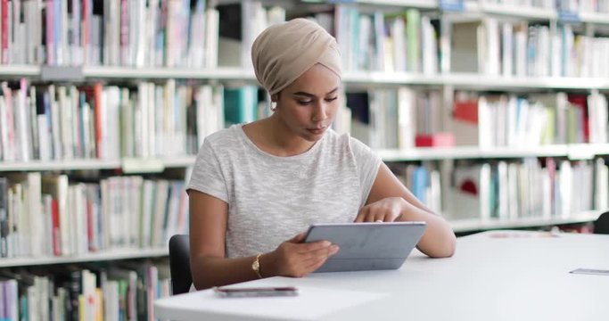 Muslim female student in college library using digital tablet