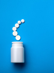 Pills spilling out of pill bottle and isolated on blue. Top view with copy space. Medicine concept