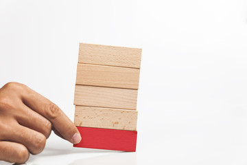 Hand holding red wooden block on the stack of wooden blocks
