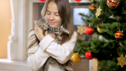 Portrait of beautiful brunette woman sitting at Christmas tree and huugging small kitten