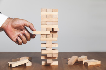 hand of businessman pulling out or placing red wood block on the tower