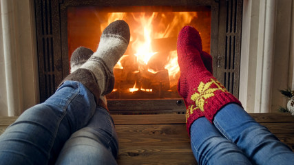 Closeup image of romantic couple and jeans and woolen socks warming by the burning fire at house