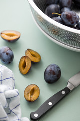 Frische, gewaschene Pflaumen Zwetschgen im Metall Sieb werden bei Küchenarbeit für Backen, Kochen, Konservieren mit Office Messer halbiert