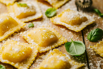 Raw ravioli with basil and flour on wooden