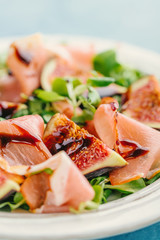 Tasty appetizing autumn salad with jamon, balsamico and figs served on plate. Closeup