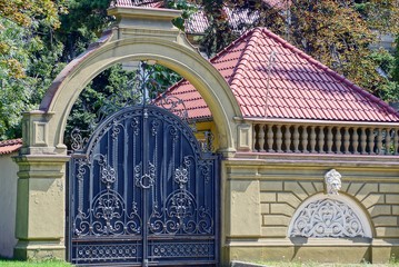 Large black iron gate with a forged pattern and a brown concrete fence