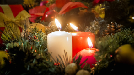 Closeup image of three burning candles and beautiful Christmas wreath