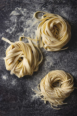 Variety of italian homemade raw uncooked pasta spaghetti and tagliatelle with semolina flour over...