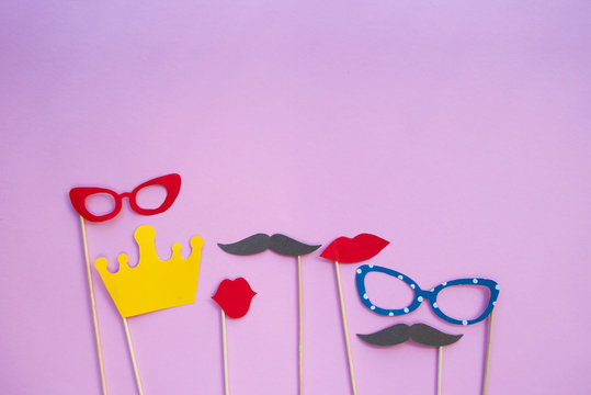 Colorful photo booth props glasses, lips, crown and moustaches on pink background with copyspace.