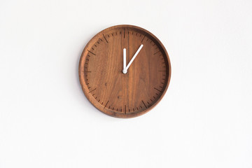 round wooden clock on white concrete wall, show time on mid day for launch time.
