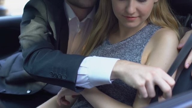 Pretty lady refusing boss harassment in auto, flirting man fastening safety belt